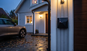 NexBlue Edge 2 laddbox monterad på villans fasad vid garaget, med en elbil parkerad framför en regnig höstkväll.
